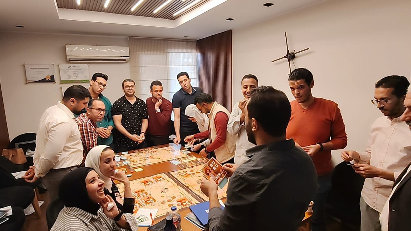 A full room laughing mid-game around the simulation board