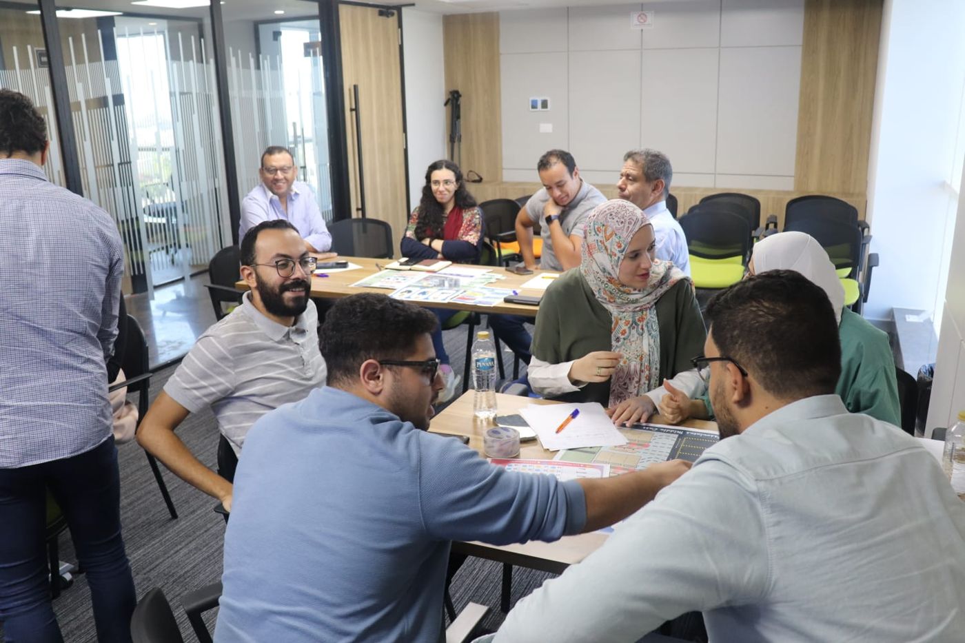 A corporate cohort playing a simulation across tables in a training room