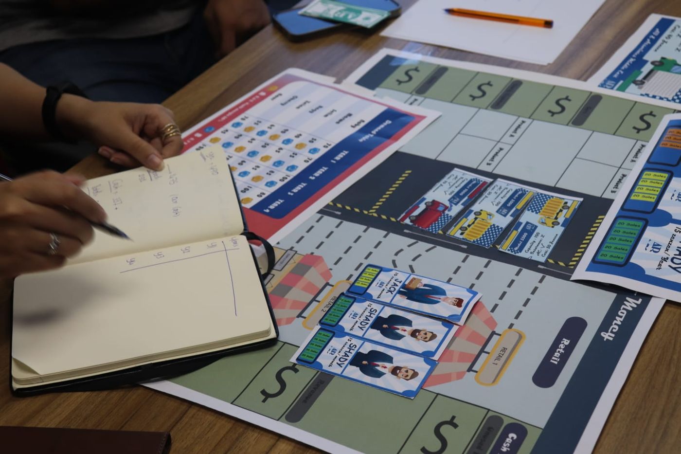 Close-up of the Psychology of Money board with employee cards, trucks and a notebook of calculations
